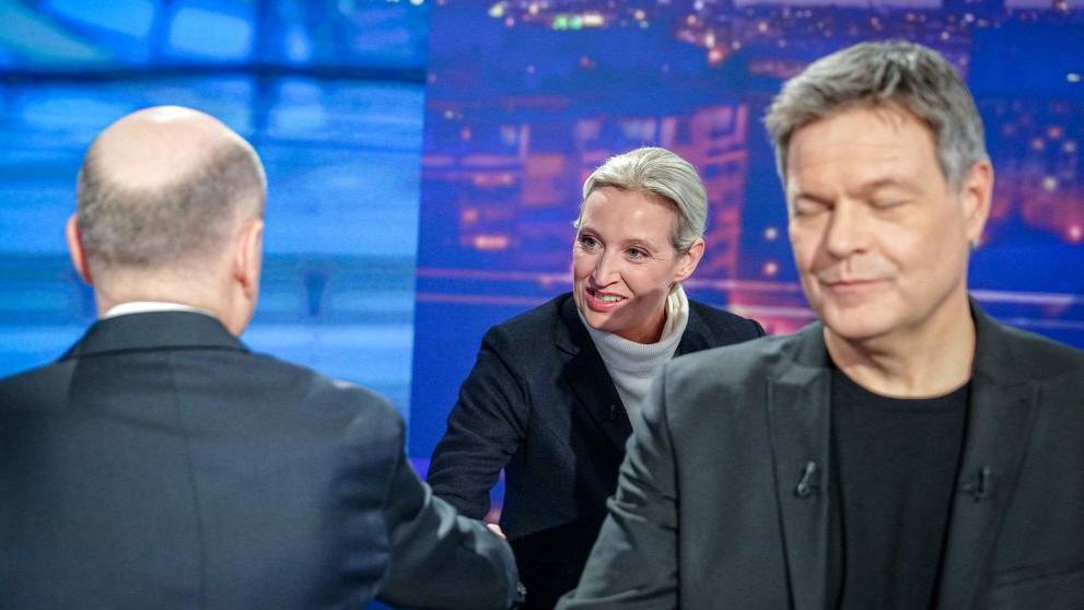 Alice Weidel leans over to shake the hand of Olaf Scholz whose back is to the camera, while the Green candidate Robert Habeck walks away