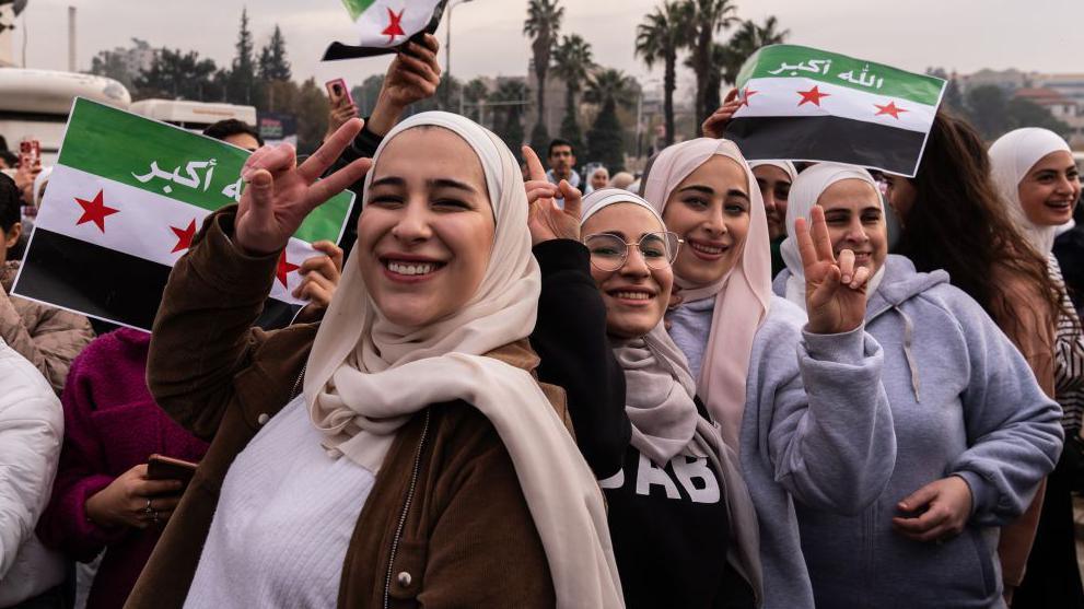 Syrians waving flags in Umayyad Square, Damascus, to celebrate the collapse of the Assad regime. Several women are making a victory sign at the camera.