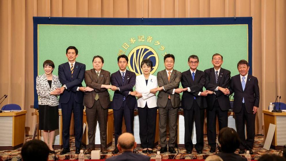 Candidates for the LDP election on stage, holding hands in a group handshake. From left to right is: Sanae Takaichi, Takayuki Kobayashi, Yoshimasa Hayashi, Shinjiro Koizumi, Yoko Kamikawa, Katsunobu Kato, Taro Kono, Shigeru Ishiba and Toshimitsu Motegi