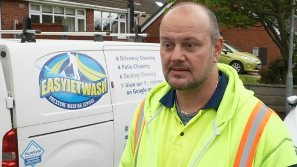 Jozsef Spekker, wearing a bright yellow jacket, standing in front of a white van with a blue and yellow Easyjetwash logo on the side.