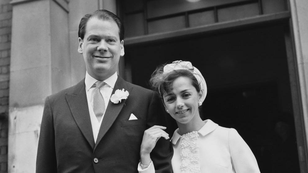 A black and white photo of the couple on their wedding day. Sir Anthony is wearing a three-piece suit with a white carnation in the button hole. Sarah is wearing a white dress and hat.