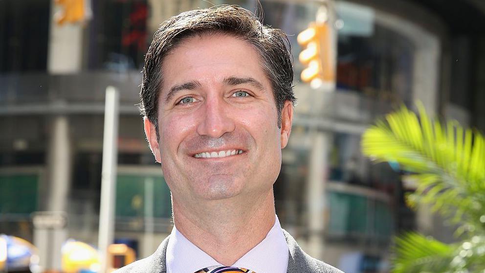 Starbucks CEO Brian Niccol standing on a New York street corner wearing a yellow, blue and white tie with a grey jacket