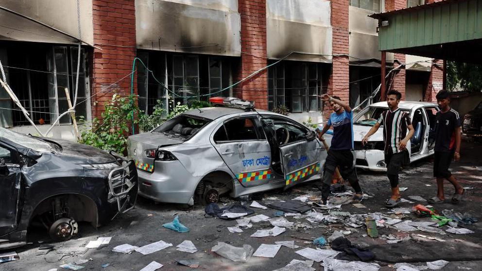 People walk next to vandalised cars at the Mohammadpur Police Station, after the resignation of Bangladeshi Prime Minister Sheikh Hasina, in Dhaka, Bangladesh, August 6, 2024.