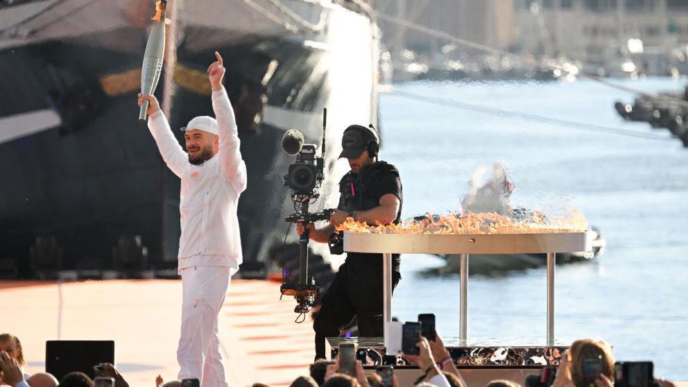 French rapper Julien Mari aka Jul holds the Olympic Torch after lighting the Olympic and Paralympic Torch Relays cauldron