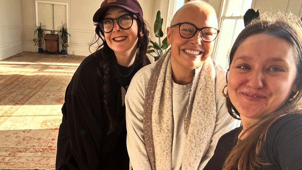 Three young woman smiling to camera in a room