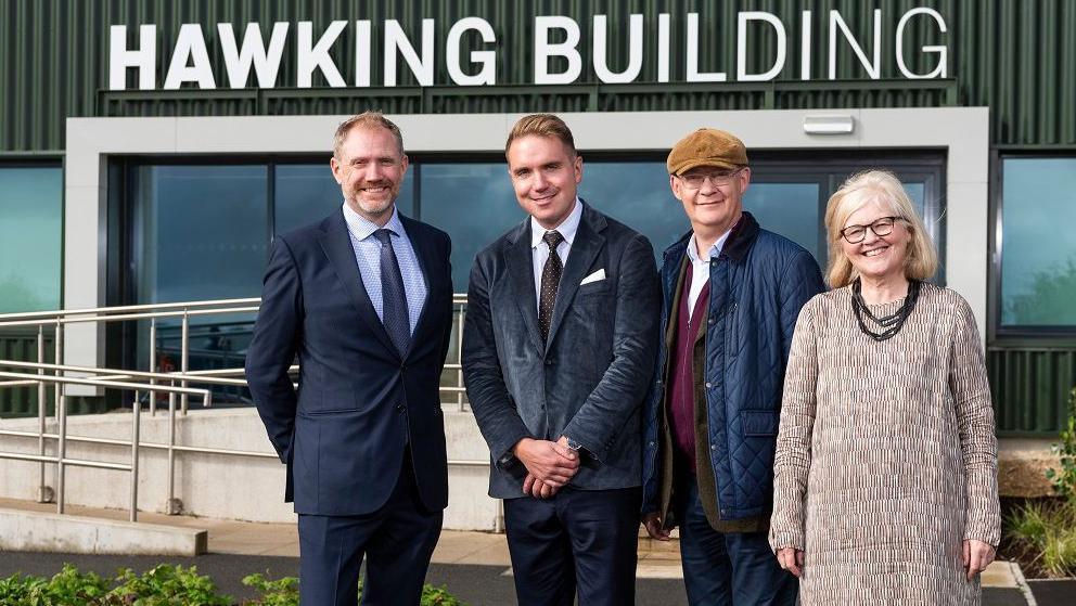 Four people in front of the building entrance - three men and a woman, with 'Hawking Building' in large lettering above the glass doors