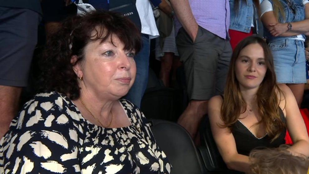 Adam Peaty's mother Caroline wearing a black and white top with Holly wearing a black top. Both women look away from the camera and towards the poolside. 