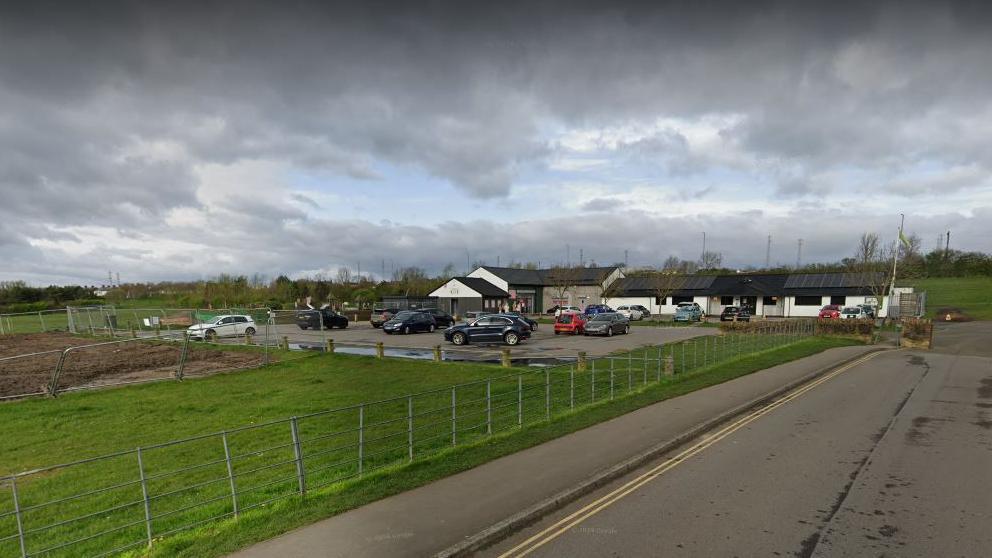 A general view of the car park at Herrington Country Park. There is a concrete car park in front of a grassed area that is fenced off and appears muddy.