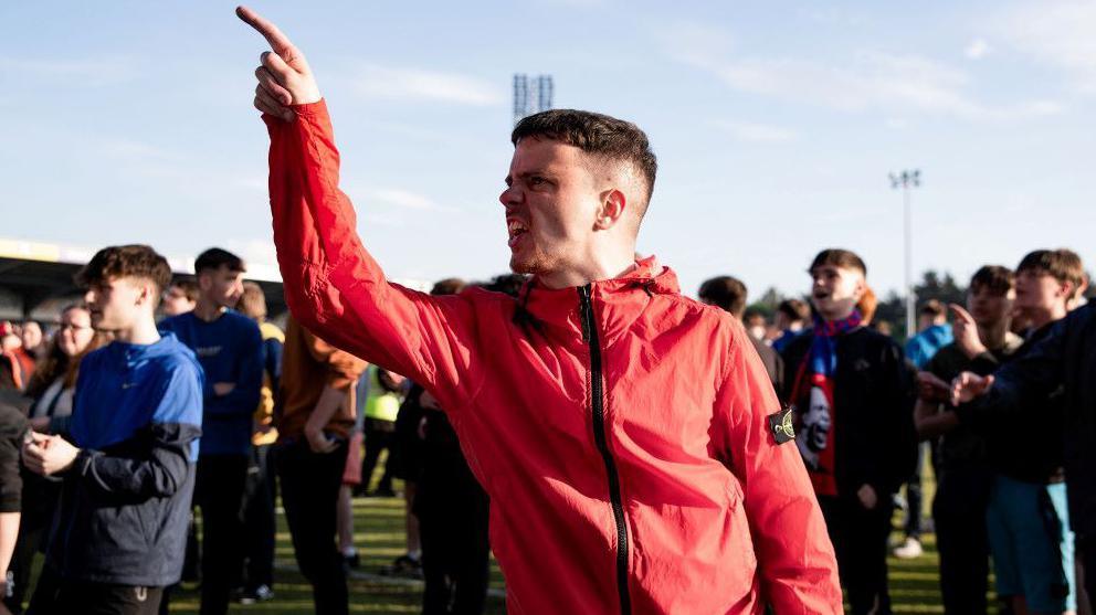 A crowd of Caley Thistle fans reacting angrily to relegation at the end of last season. One fan gestures angrily.