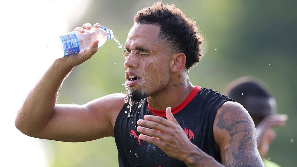Noah Okafor pours water over his face to cool down during an AC Milan training session