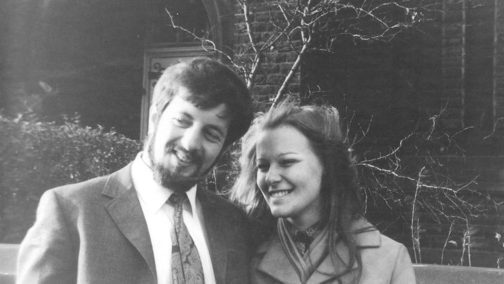 A black-and-white image of a young Barrie and Muriel. He wears a suit and has dark hair and a beard. She has long dark hair and wears a coat.