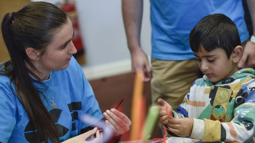 A boy is shown with an art worker at a craft session