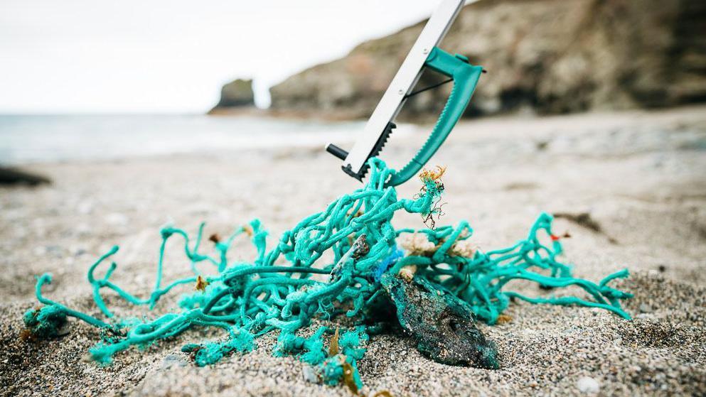 A piece of green discarded fishing net on a beach being picked up by a litter-picker