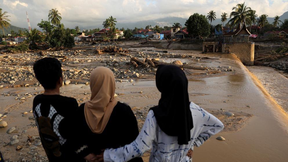 Two women in Muslim headscarves and a man look at muddy ground strewn with stones.