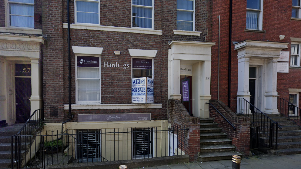 Terraced building with the sign "Hardings" at the front. There are also "For Sale" hoardings attached to the terraced building. 