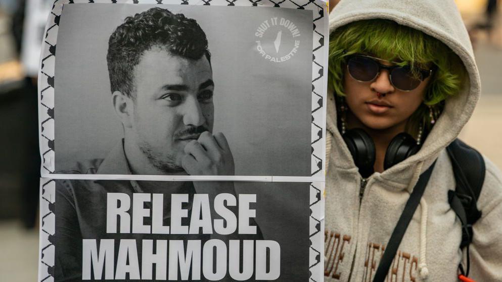 A protester in New York City with green hair and sunglasses holds up a sign that reads: "RELEASE MAHMOUD"