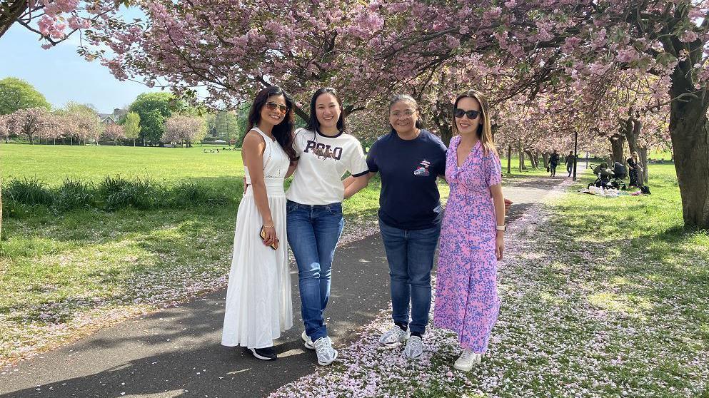 Four women stand on a path on a park in Harrogate, underneath cherry blossom trees.