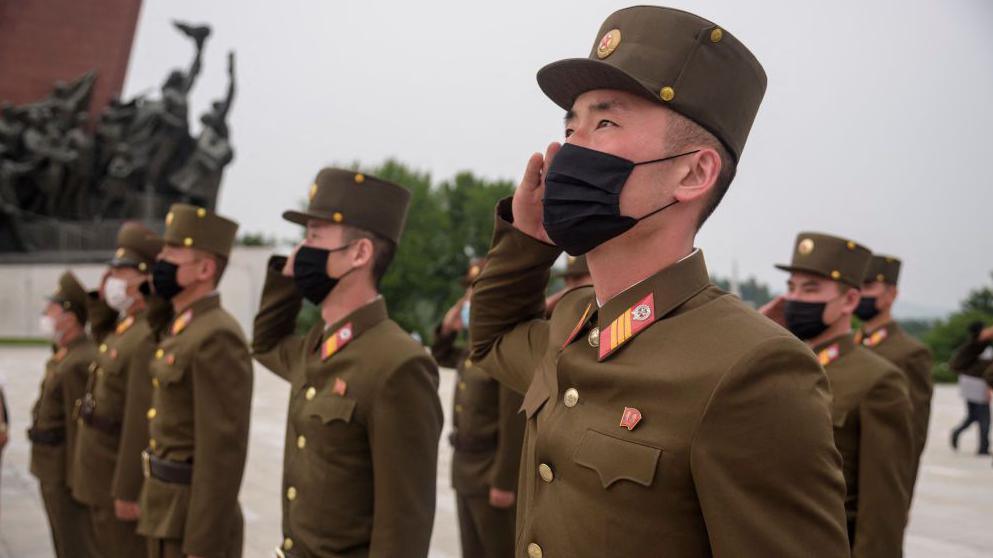 North Korean soldiers wearing facemasks salute as they pay their respects to the country's former leaders in 2021