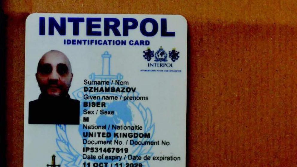 Fake Interpol ID in the name of Biser Dzhambazov. 

The card is white with a photo of a bald-headed man in a black jumper on the left. On the right is information including sex and nationality, which is listed as United Kingdom, 

The card is on a wooden surface.