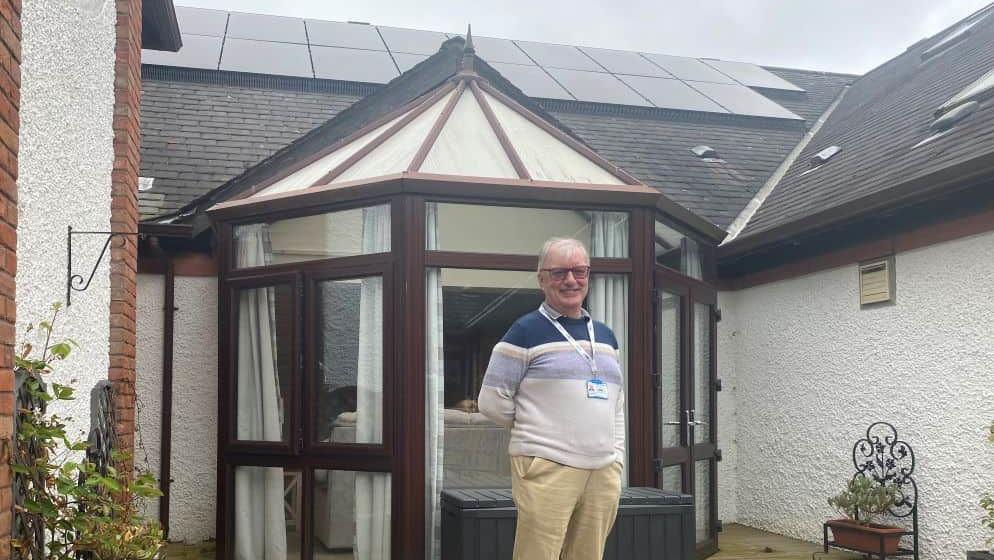 James Porter standing in front of the entrance to the hospice, On the roof above him you can see the solar panels 