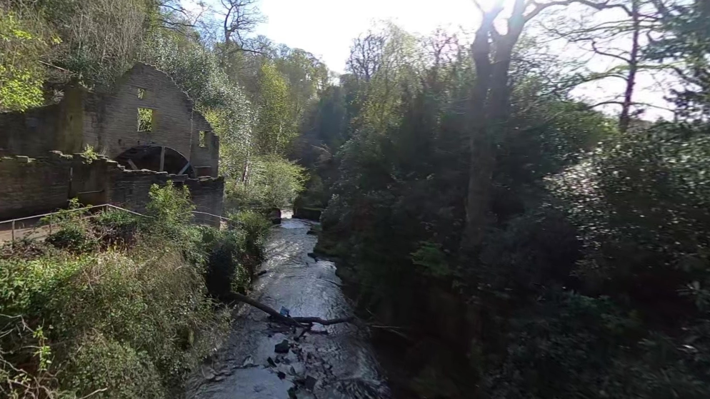 A river surrounded by trees and bushes. A ruin of a stone mill can be seen to the left.