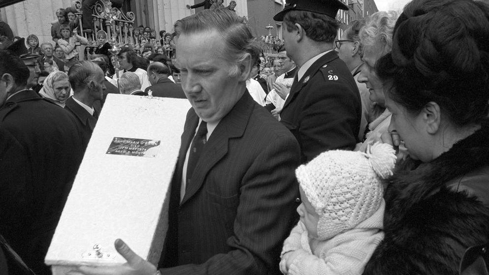 A man holding the white coffin of Baby Anne Marie O'Brien