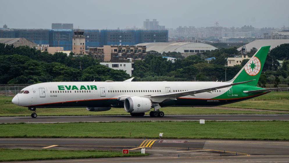 Wide shot of EVA AIR jet with white and green livery is shown at Taoyuan Airport in Taiwan, with a city skyline in the background