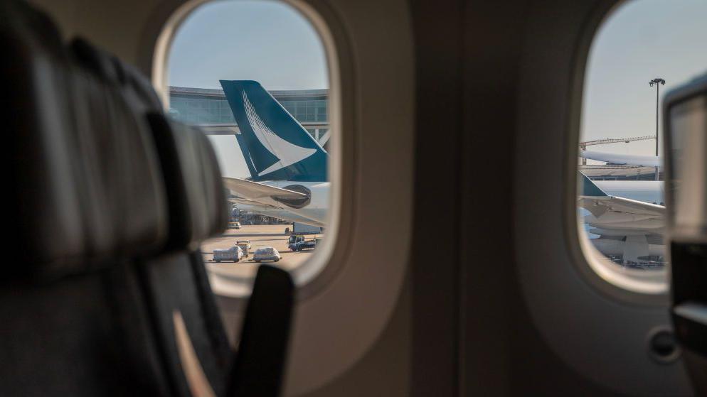 A view from inside an airplane cabin shows the tail of a Cathay Pacific plane at Hong Kong International Airport