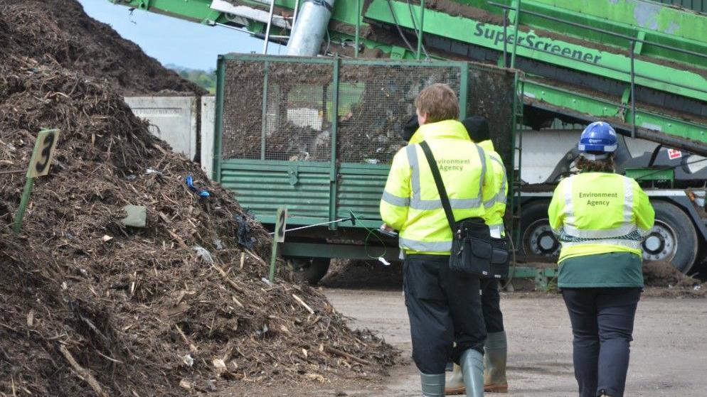 Environment Agency officers in high-vis jackets standing next to a pile of compost.