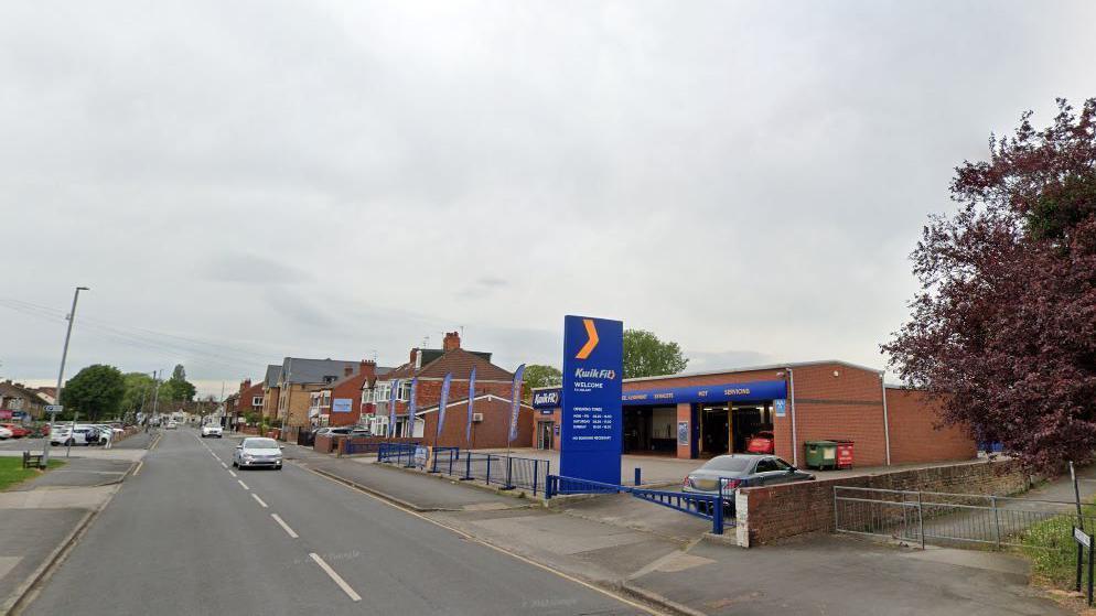 A Google Street View of Hull Road, Anlaby. There are paths on both sides of the road. A Kwik Fit branch is on the right and there are houses in the distance.