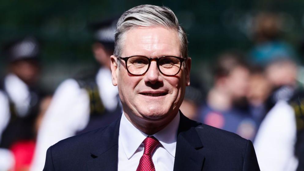 Sir Keir Starmer smiling at the camera wearing a navy blazer, white shirt and red tie.