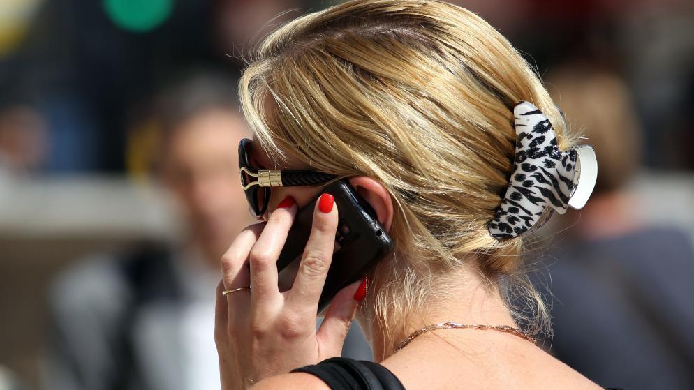A woman with blonde hair and sunglasses can be seen holding a mobile phone to her ear.