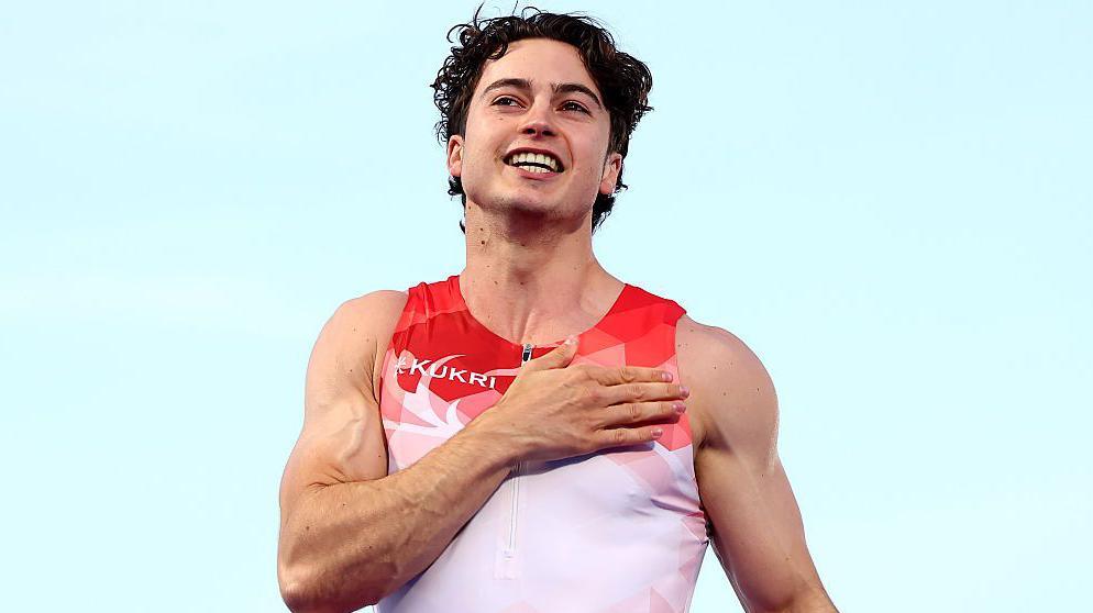 A smiling Owen Heard with his right hand on his chest wearing a red and white Team England vest