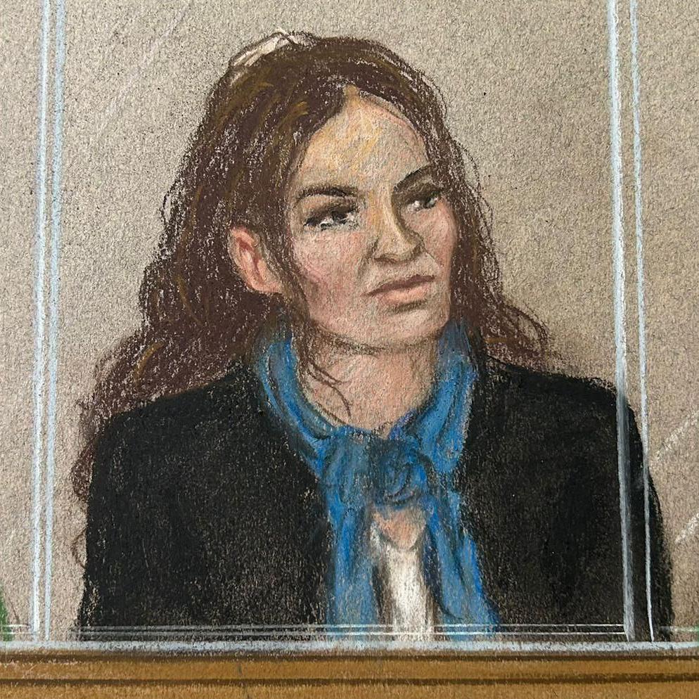 Constance Marten, a woman with long dark-brown hair who is wearing a black jacket with a blue scarf and white top, sitting behind glass in a court dock