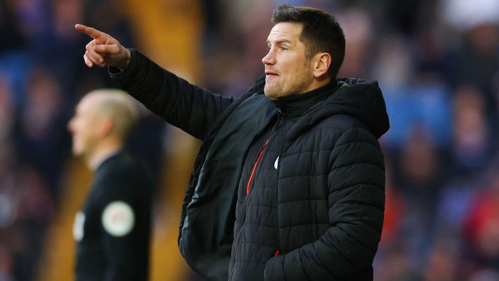 Crewe Alexandra manager Lee Bell stands on the touchline in his club puffer coat pointing and shouting instructions