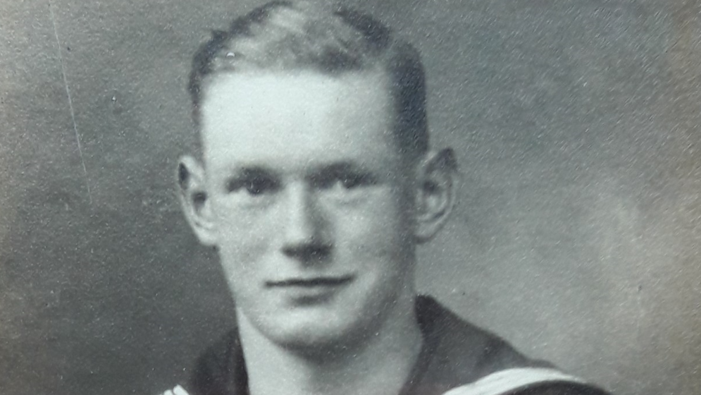 A young man with short hair in Navy uniform against a grey background