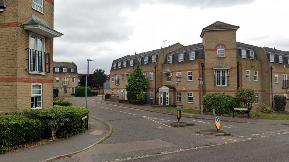 Three-storey flats or houses are visible in Howard Close, which is a residential cul-de-sac. It is a cloudy day.