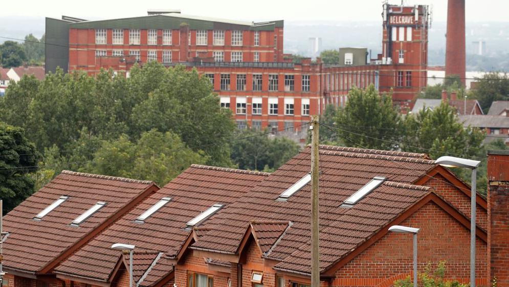 Terrace housing, including a row of residential houses, homes and rooftops in the town of Oldham, with a mill building seen in the background. 