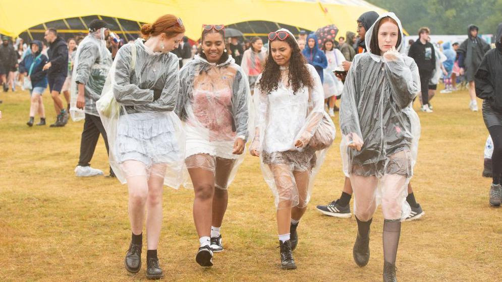 Four women walk through the Reading crowd wearing rainproof outer clothing.