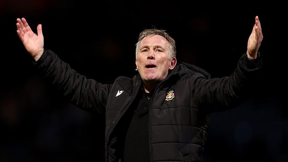 Phil Parkinson with arms outstretched in a black jacket celebrating Wrexham's win at Loftus Road