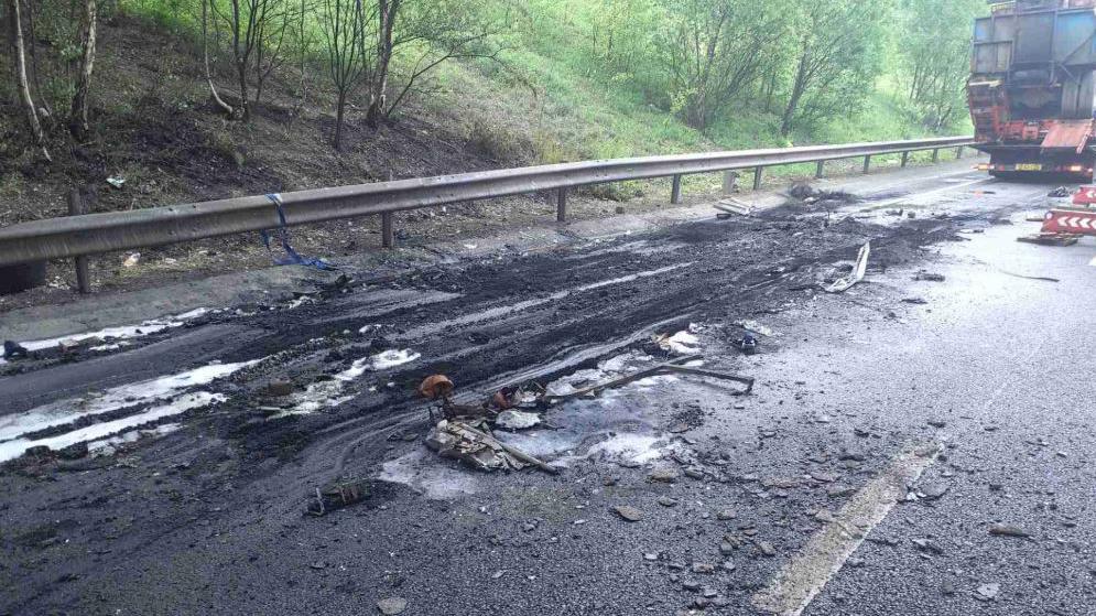 Charred debris across road surface with resurfacing lorry on the far right.