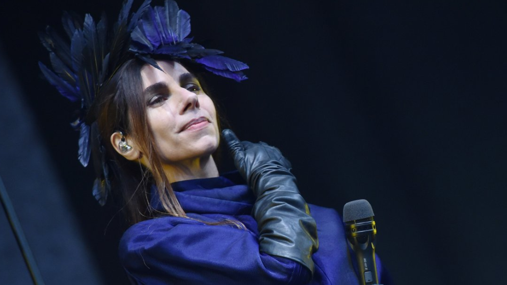 PJ Harvey on stage wearing a dark blue top with blue feathers in her hair.