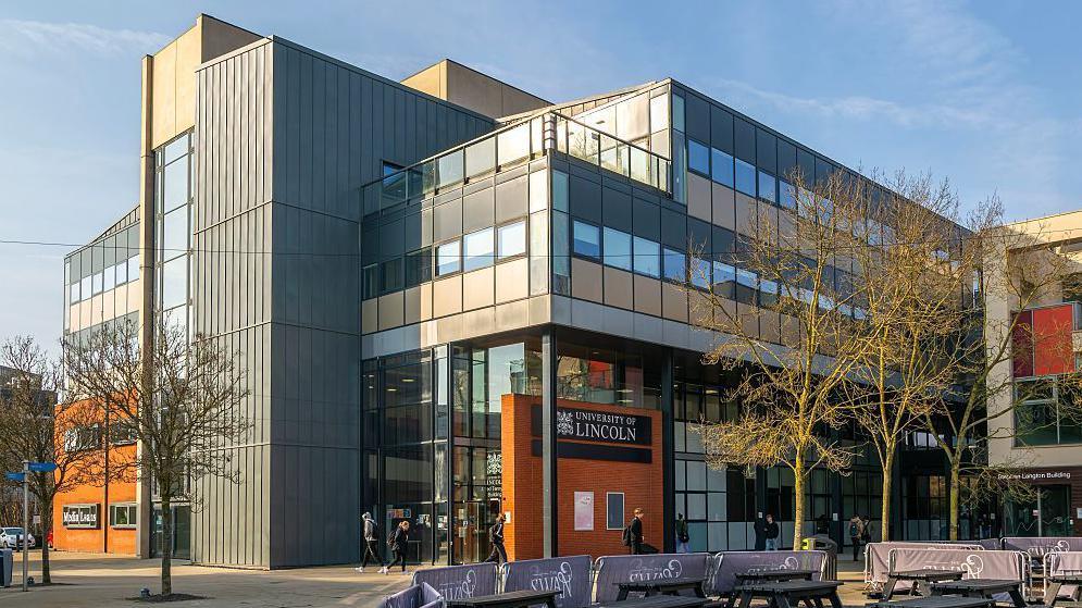 A general shot of the University of Lincoln's Alfred Tennyson Building, which is a modern-looking, multi-storey, grey and orange building looking on to an open square.