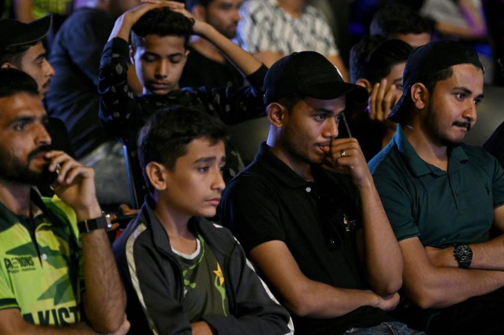 Cricket fans react as they watch a live broadcast of the ICC Champions Trophy one-day international (ODI) cricket match between India and Pakistan in Dubai, on a big in Karachi on February 23, 2025