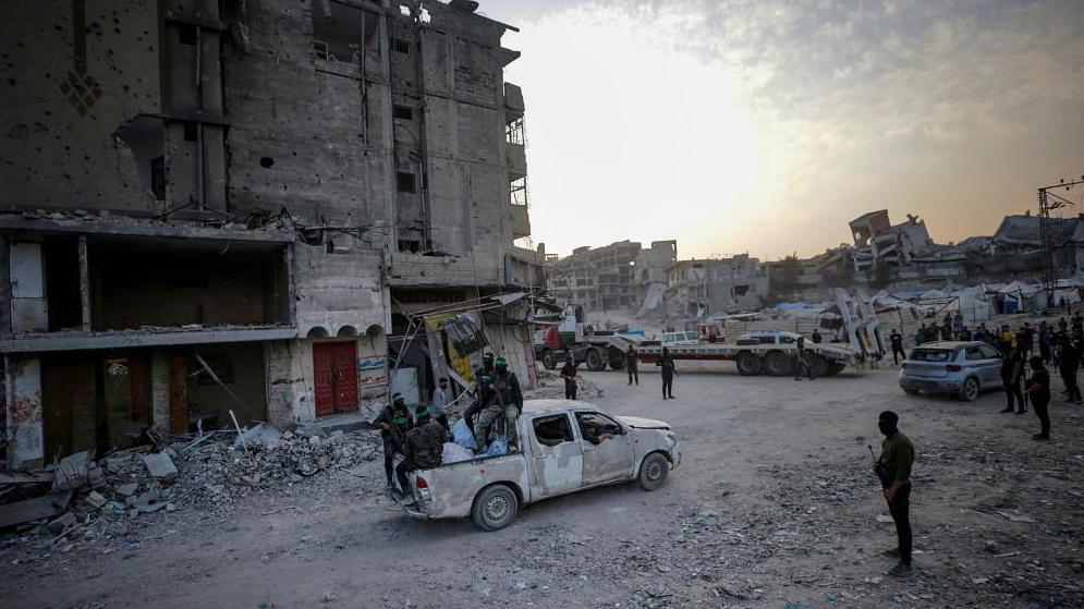 Hamas fighters sitting in the back of a van with destroyed buildings behind them