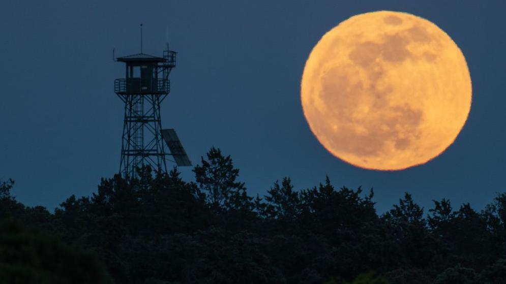 The full moon of April known as the Pink Moon rises over a fire lookout tower. 