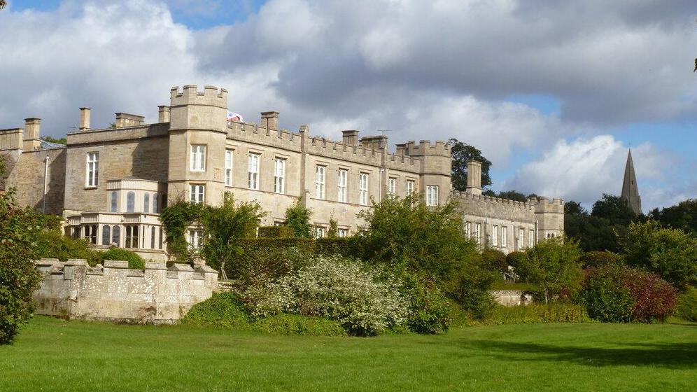 Deene Park, a castellated, grey stone two-storey stately home, raised above a lawn 