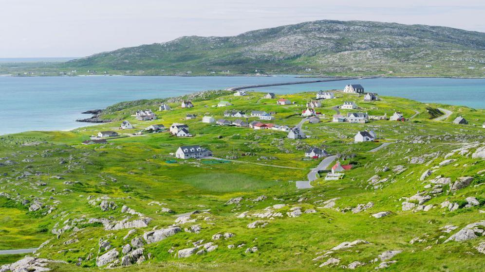 White-walled houses are scattered across a rocky landscape by the sea.