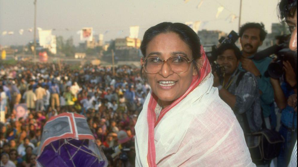 Awami League ldr. Sheik Hasina Wazed on stump, holding party campaign item, during crowded election campaign rally, in a picture dated from 1991.