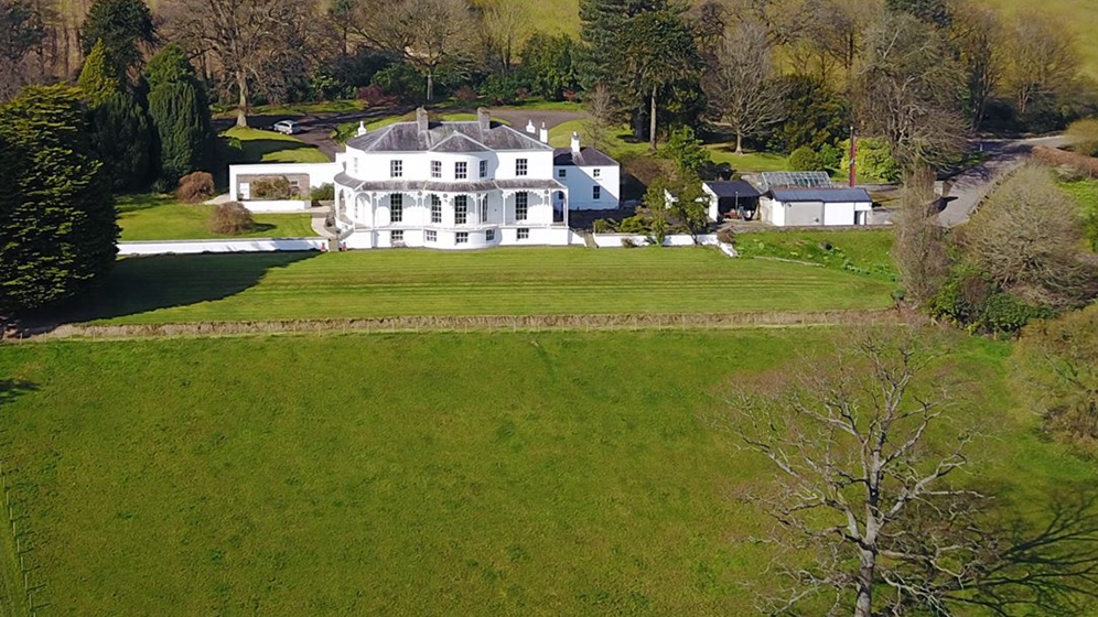 Shows a large white mansion surround by trees 